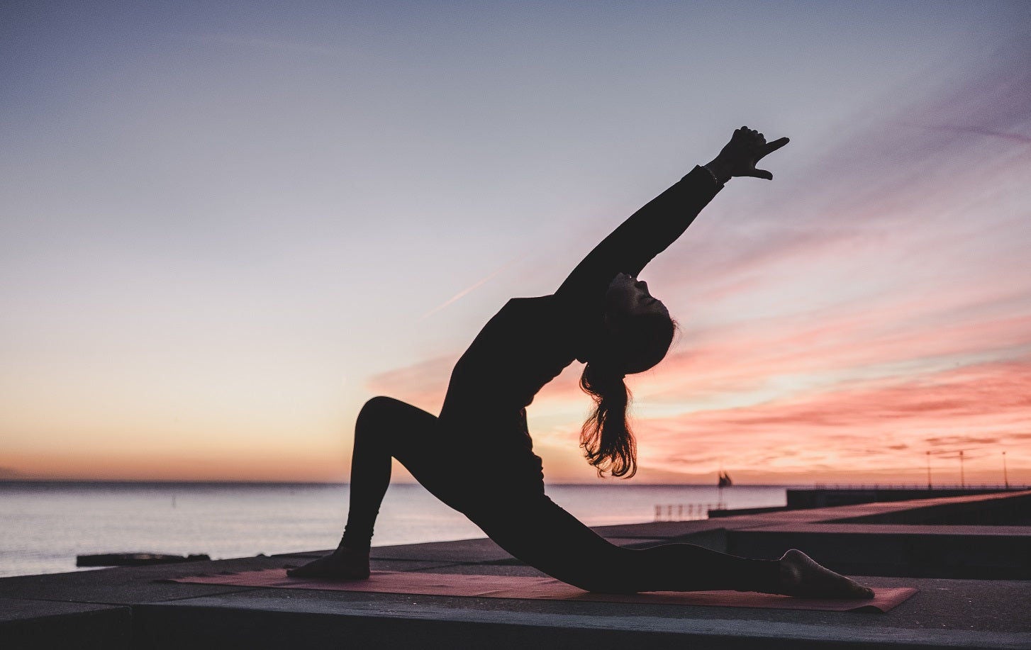 Silhouette of woman practicing yoga at sunset